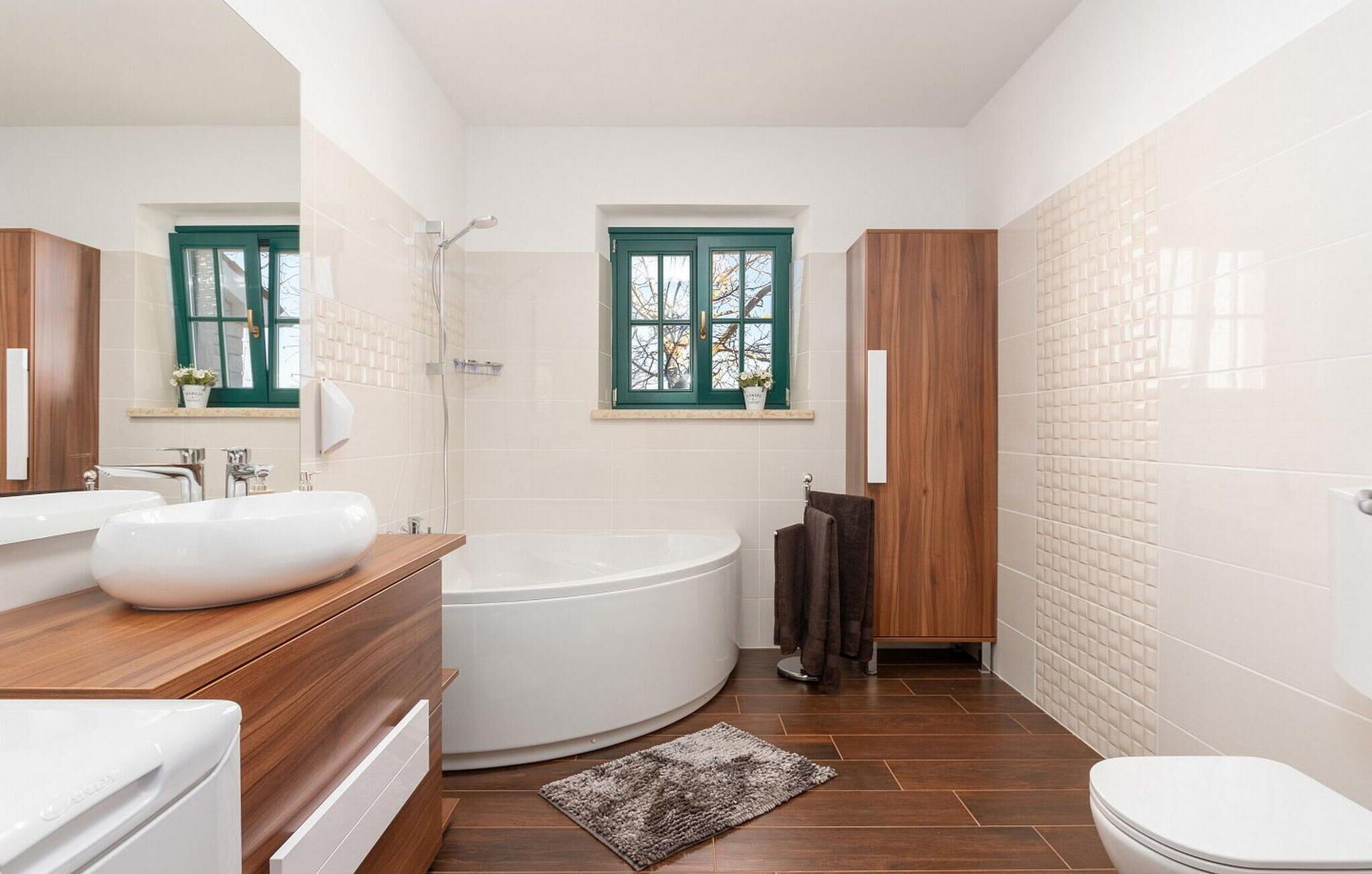 A modern bathroom with a freestanding bathtub, a large mirror, and a window with green shutters.