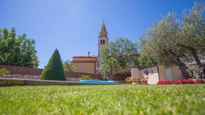Un quartier résidentiel avec un ciel d’un bleu éclatant, un clocher d’église imposant, une pelouse parfaitement entretenue et une petite piscine.