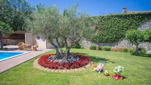 Un jardin avec une piscine, un arbre entouré de fleurs rouges et un mur de pierre recouvert de lierre.