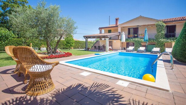 Une piscine avec des chaises longues, un patio couvert et une maison avec un toit en tuiles.