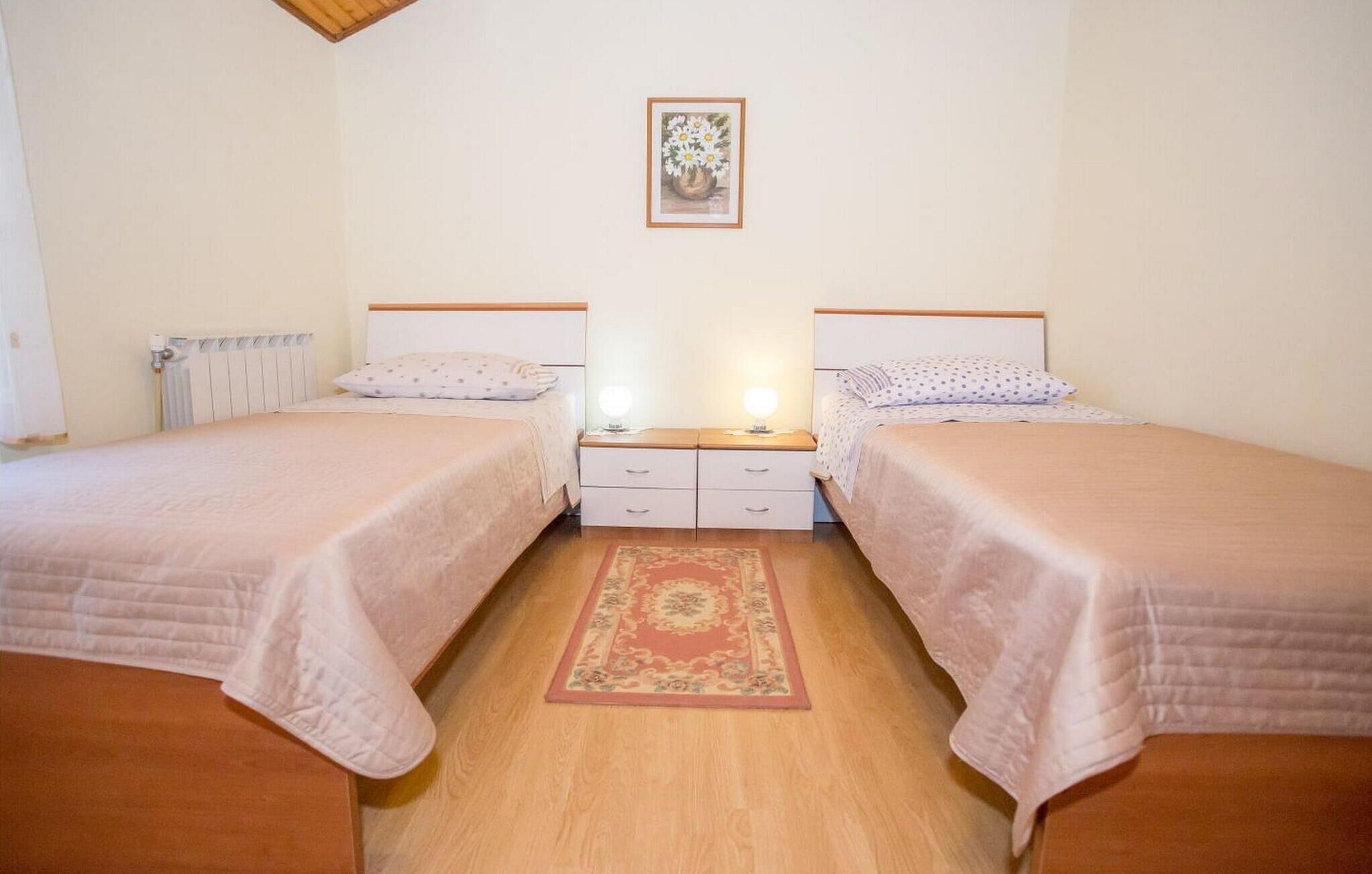 A bedroom with two beds, a nightstand, a radiator, and a framed picture on the wall.