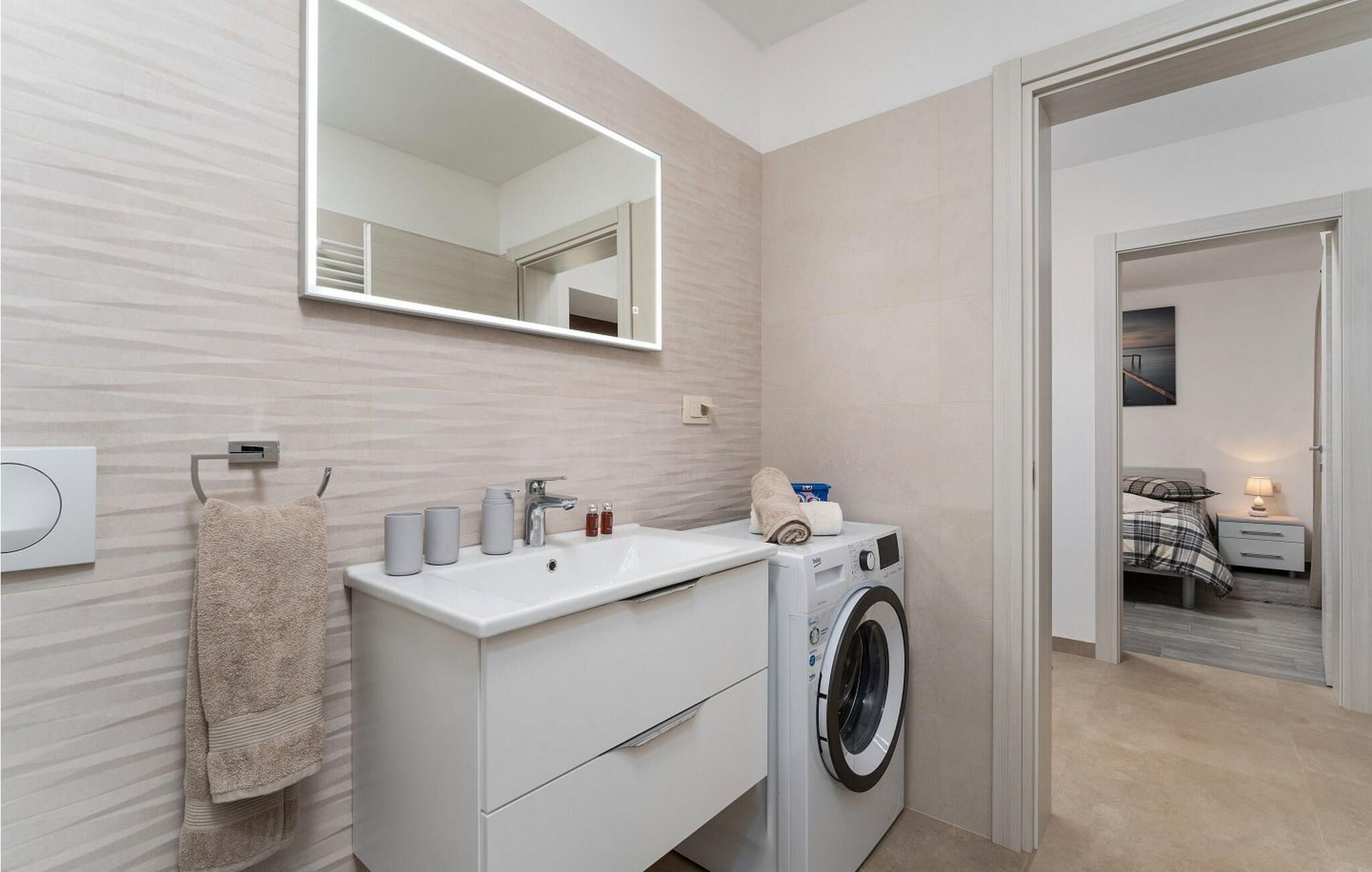 A modern bathroom with a built-in washing machine, a large mirror, and a towel rack.