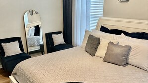 A bedroom with a large bed, a dresser, a mirror, and a window with blinds. - Located in the heart of Houston! Easy access to freeways, sports arenas, & more! (Houston)