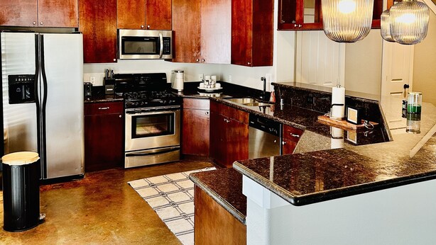 A modern kitchen with stainless steel appliances, wooden cabinets, and pendant lighting. - Located in the heart of Houston! Easy access to freeways, sports arenas, & more! (Houston)