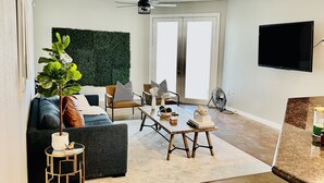 A modern living room with a sofa, coffee table, and a plant. - Located in the heart of Houston! Easy access to freeways, sports arenas, & more! (Houston)