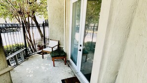 A covered outdoor area with a sliding glass door, a small table, and a bench. - Located in the heart of Houston! Easy access to freeways, sports arenas, & more! (Houston)