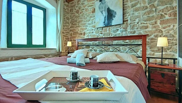 Une chambre avec un mur en pierre, un lit avec une tête de lit, une fenêtre et un plateau avec des tasses à café.