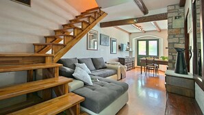 Un vaste espace de vie agrémenté d’un escalier en bois, d’un canapé gris, d’une table à manger et d’un mur en pierre.