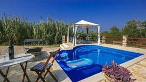 Une piscine avec un espace de détente, un coin salon couvert et une table avec une bouteille et un verre.