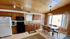 A kitchen with wooden cabinets, a refrigerator, a stove, and a dining area with a table and chairs. - Cabin 9 Lakefront Family Resort (Hines)