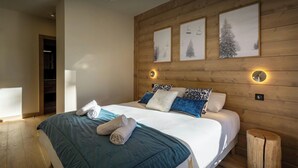 A modern bedroom with a wooden headboard, a large bed with blue bedding, and three framed pictures on the wall.