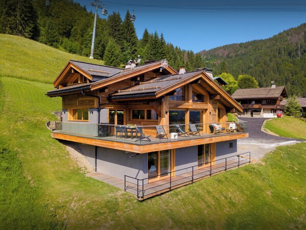 A modern log cabin with a balcony, large windows, and a ski lift in the background. - Chalet Fernand - La Clusaz stylish stay for 10 with spa - OVO Network (La Clusaz)