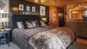 A bedroom with a large bed, wooden walls, framed pictures, and a mirror above the dresser.