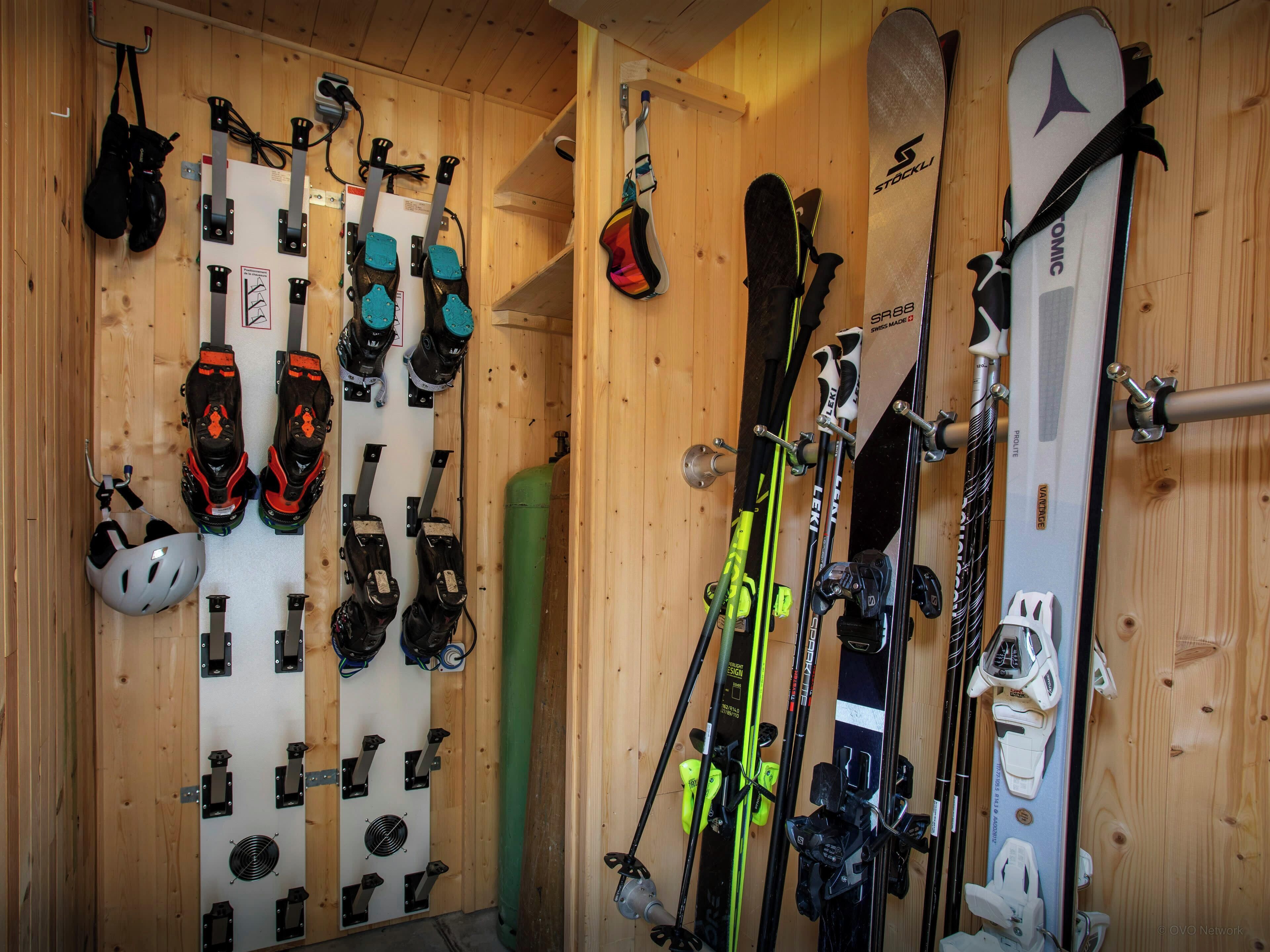 A ski storage room with skis, ski boots, and helmets organized on racks.