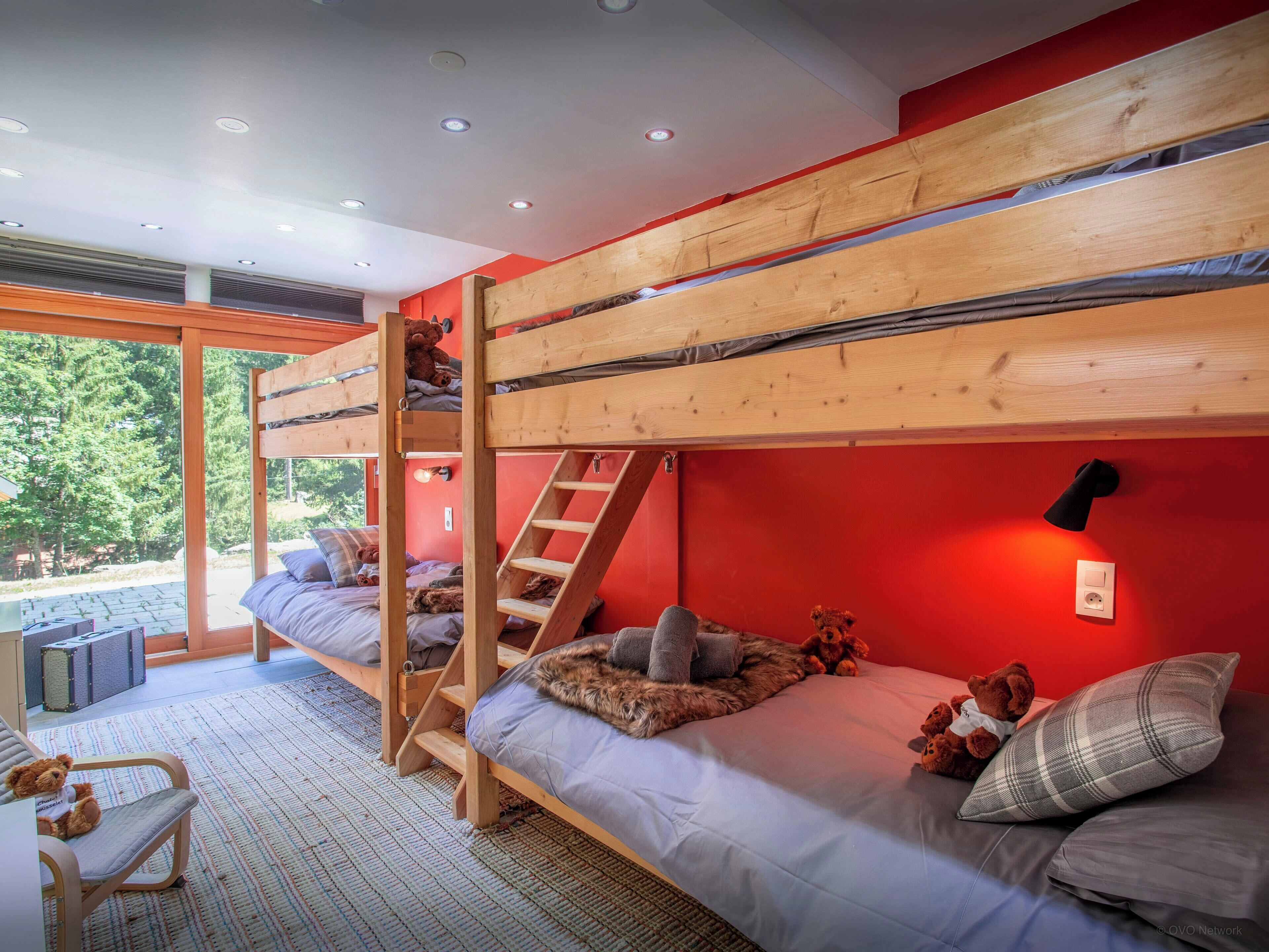 A bunk bed room with a ladder, a window, and a teddy bear on the bed.