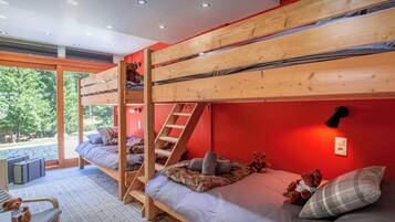 A bunk bed room with a ladder, a window, and a teddy bear on the bed.