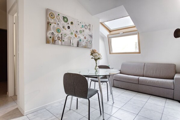 Una sala de estar moderna con una mesa de vidrio, sofá gris y un tragaluz en el techo.