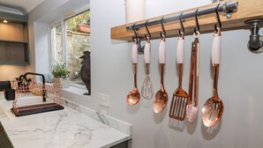 A kitchen with a marble countertop, a copper utensil rack, and a window with a view of greenery. - Golygfa Bryn (Porth)