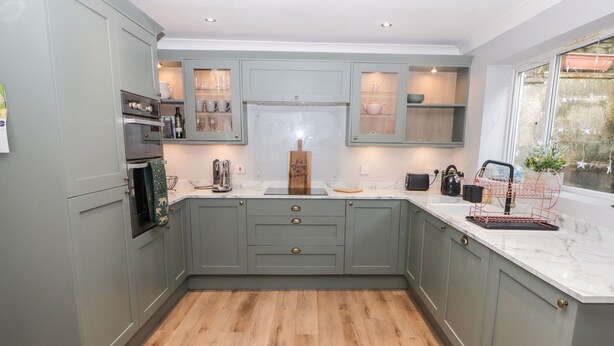 A modern kitchen with grey cabinets, wooden flooring, and a marble countertop. - Golygfa Bryn (Porth)