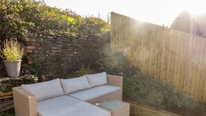 A wicker sectional sofa with cushions, a small table, and a stone wall in the background. - Golygfa Bryn (Porth)