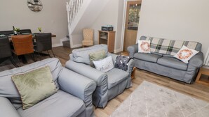 A modern living room with grey sofas, a wooden staircase, and a dining area with chairs and a table. - Golygfa Bryn (Porth)