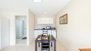 Een kleine keuken met witte kastjes, een magnetron en een broodrooster. Er staat een eettafel met borden en een fles.