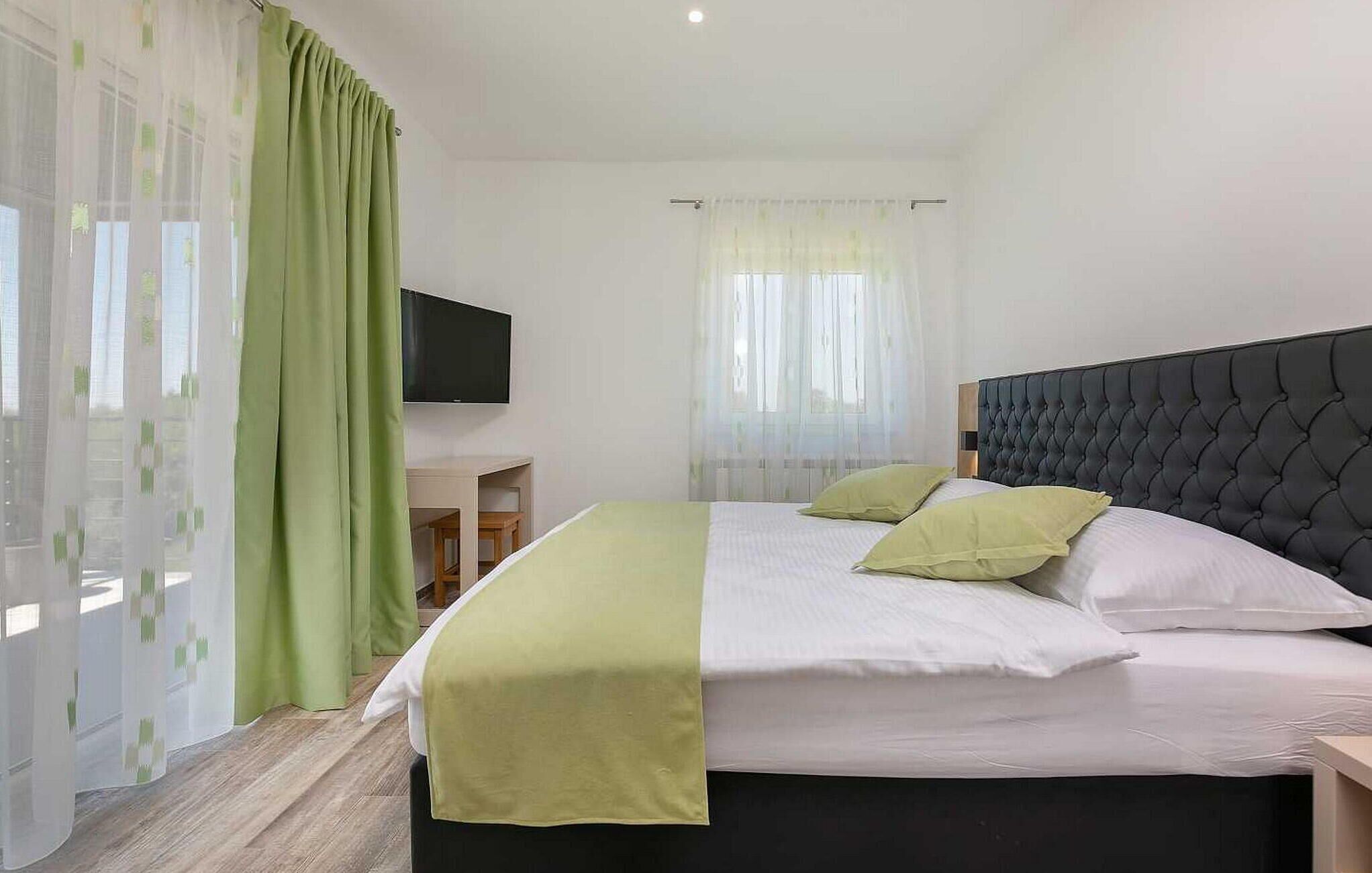 A hotel room with a bed, a TV mounted on the wall, and a desk with a chair.