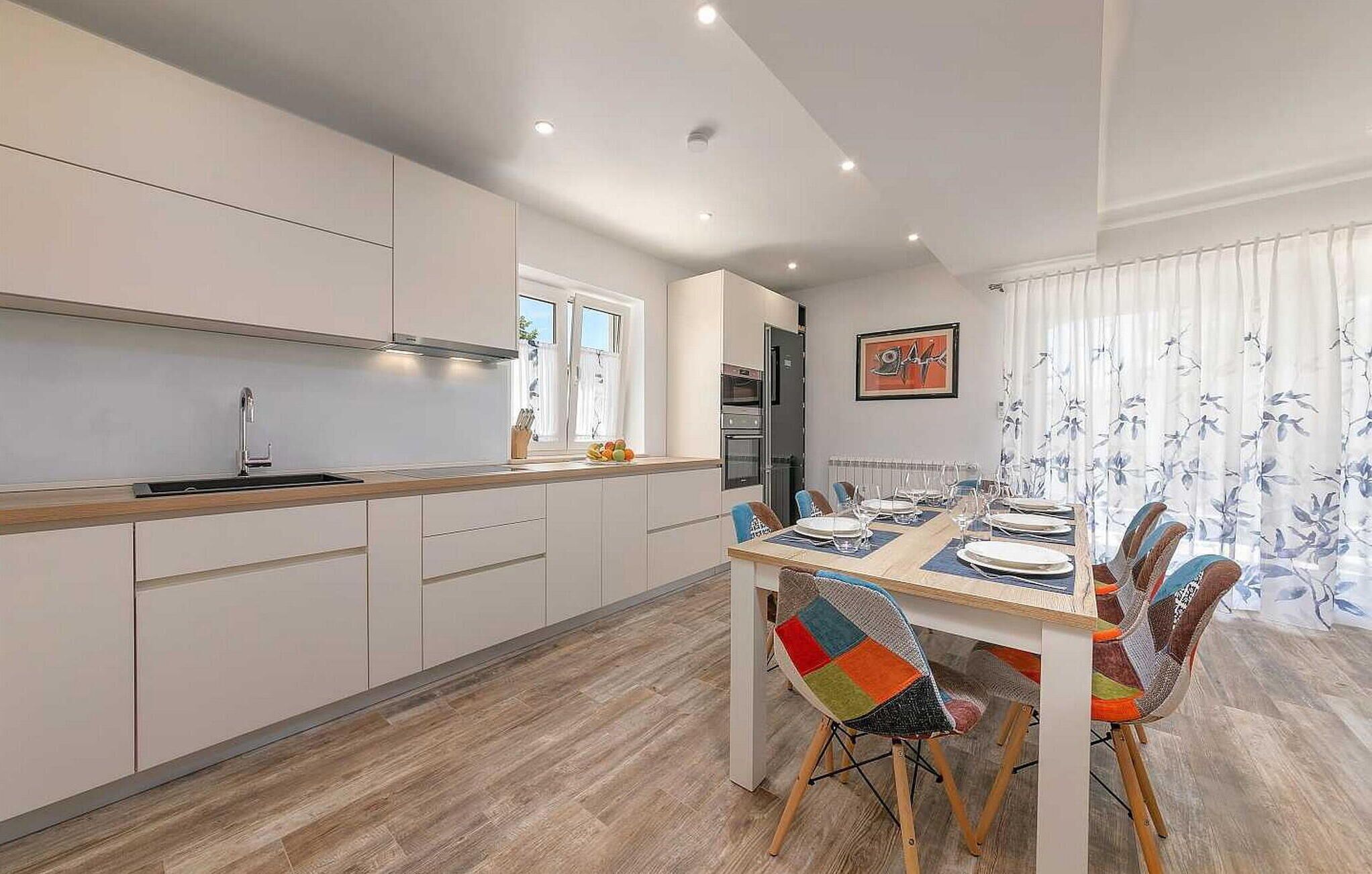 Una cocina moderna con armarios blancos, encimera de madera y un comedor con mesa dispuesta para cuatro.