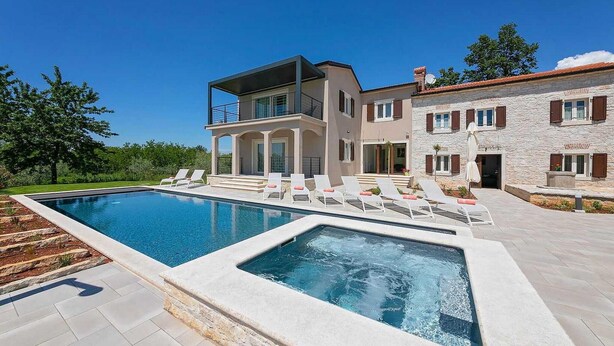 Ein modernes, zweistöckiges Haus mit Swimmingpool, Liegestühlen und einer Fassade aus Naturstein.