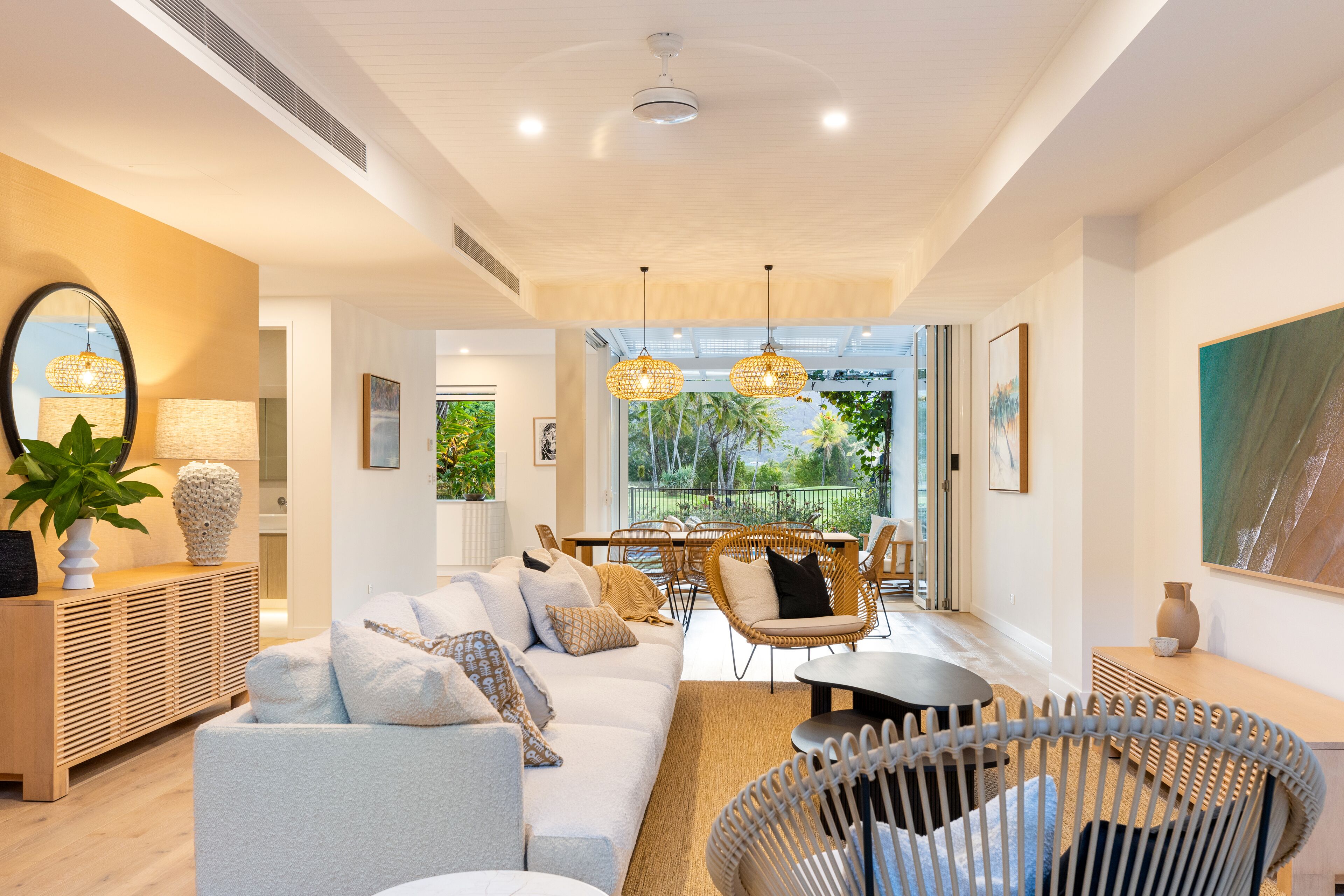 A modern living room with a sofa, chairs, a dining table, and a large window with a view of greenery.