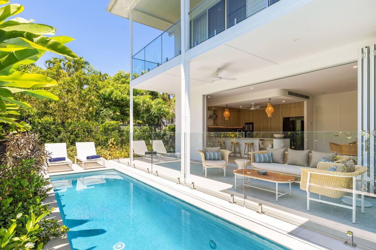 Ein modernes Haus mit Pool, Glasgeländern und Gartenmöbeln.