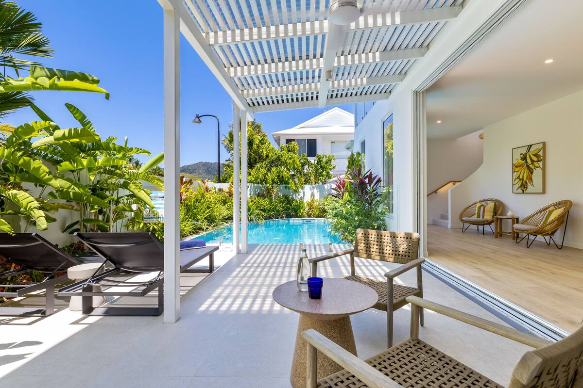 Ein sonniger Außenbereich mit Pool, Liegestühlen und einem Tisch.