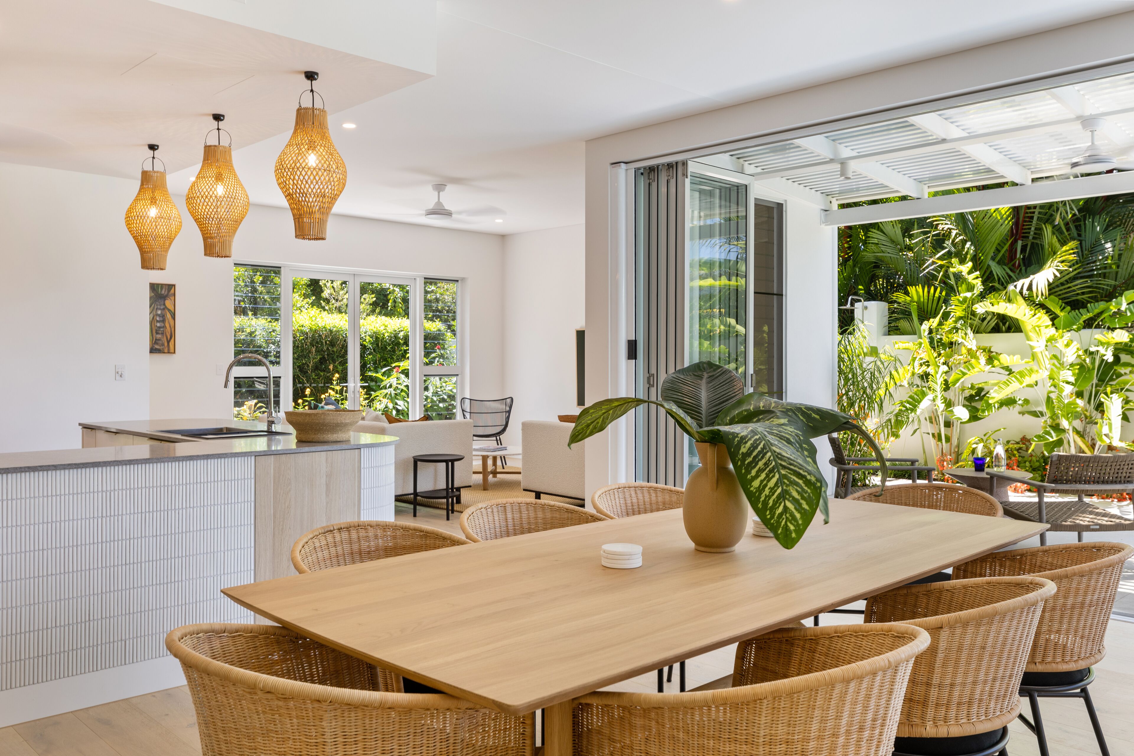 Une cuisine moderne dotée d’un grand îlot central, de meubles en osier et offrant une vue sur une végétation luxuriante.