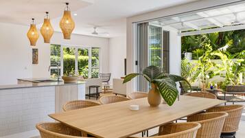 Une cuisine moderne dotée d’un grand îlot central, de meubles en osier et offrant une vue sur une végétation luxuriante.