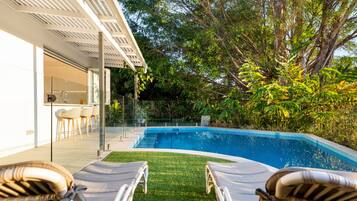 A swimming pool with lounge chairs, a glass door entrance, and a garden area with trees and plants.