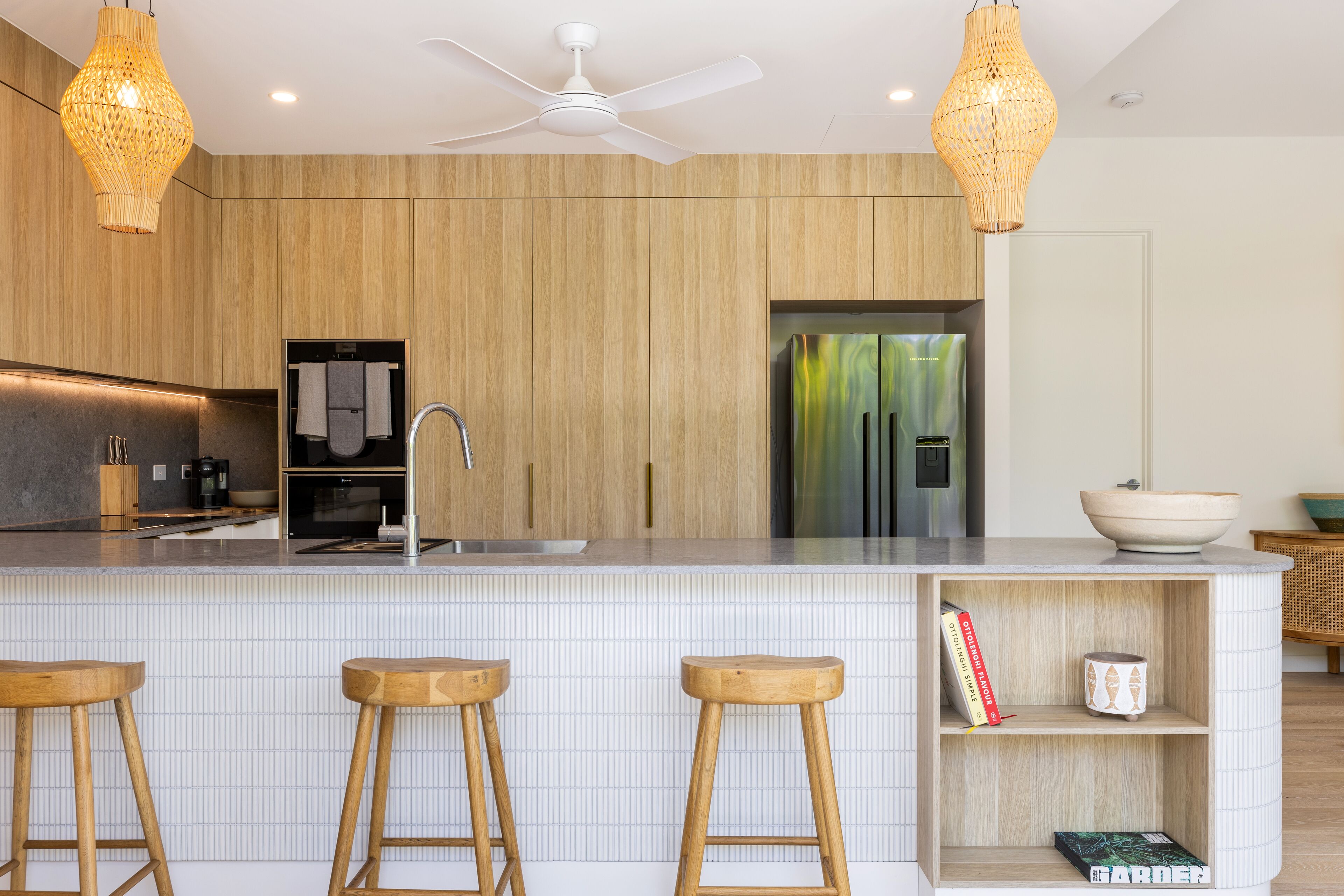 A modern kitchen with wooden cabinetry, a white tiled backsplash, and a central island with stools.