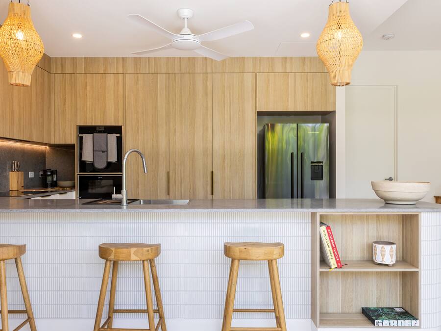 A modern kitchen with wooden cabinetry, a white tiled backsplash, and a central island with stools.