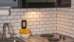 Een keuken met een zwarte magnetron, een gasfornuis, een spoelbak en een schaal met citroenen.