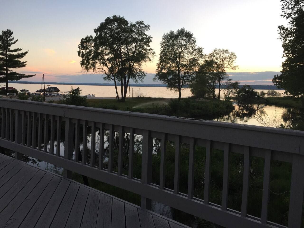 Eine Holzterrasse mit Blick auf ein Gewässer, Bäume und eine entfernte Küste.