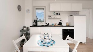 Une cuisine compacte avec des meubles blancs, une machine à café et une table à manger avec des chaises.