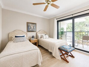 Ein Schlafzimmer mit zwei Betten, einem Deckenventilator, einem Fenster mit Blick ins Freie und einem kleinen Tisch mit einer Lampe.