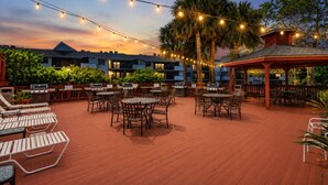 An outdoor patio area with multiple barbecue grills, tables, and chairs, surrounded by palm trees and string lights. - Park Shore Resort-Top Floor BLDGC #221*Peaceful* (Park Shore Resort)