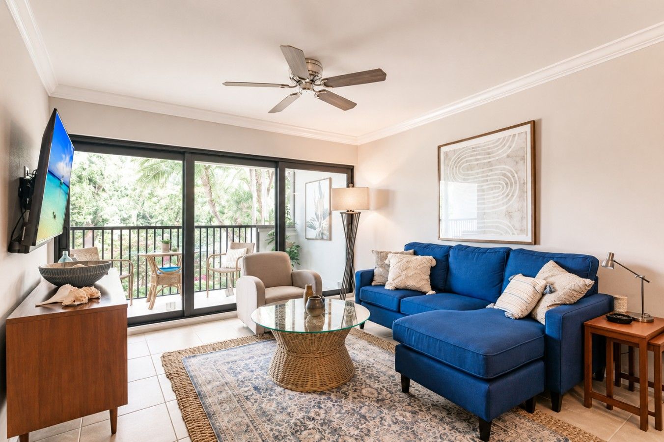 A living room with a blue sofa, a glass coffee table, a television, and a ceiling fan.