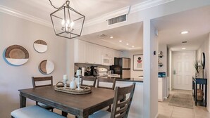 A dining area with a wooden table and chairs, a chandelier, and wall decor. - Park Shore Resort-Top Floor BLDGC #221*Peaceful* (Park Shore Resort)