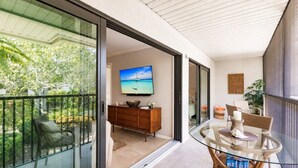 Un balcon avec une table et des chaises en verre, un meuble en bois et un téléviseur diffusant une vue panoramique.