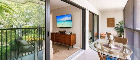A balcony with a glass table, wicker chairs, and a television in the background.