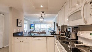 A modern kitchen with white cabinetry, a granite countertop, a built-in dishwasher, a microwave, and a stove. - Park Shore Resort-Top Floor BLDGC #221*Peaceful* (Park Shore Resort)
