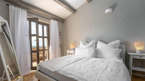 Un dormitori amb un llit gran, cortines blanques, un terra de fusta i vista a través d'una porta de vidre.