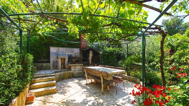 A garden patio with a stone table and steps leading to a small stone structure.