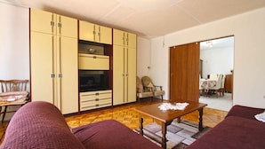A living room with a sofa, a wooden coffee table, and a TV. There is a wooden cabinet and a chair.